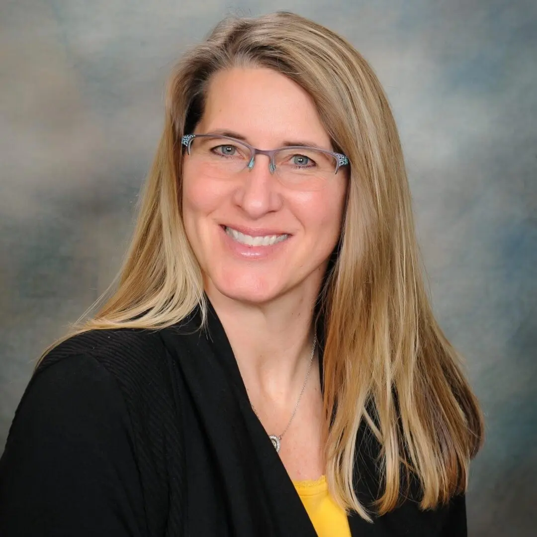 A woman with long blonde hair wearing glasses.