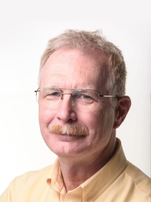 A man with glasses and a mustache wearing a yellow shirt.