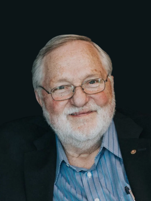 A man with white hair and glasses wearing a suit.